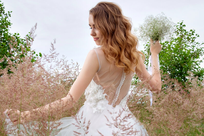 Woman with her hair curled all down in a wedding dress outdoors, holding a small bouquet